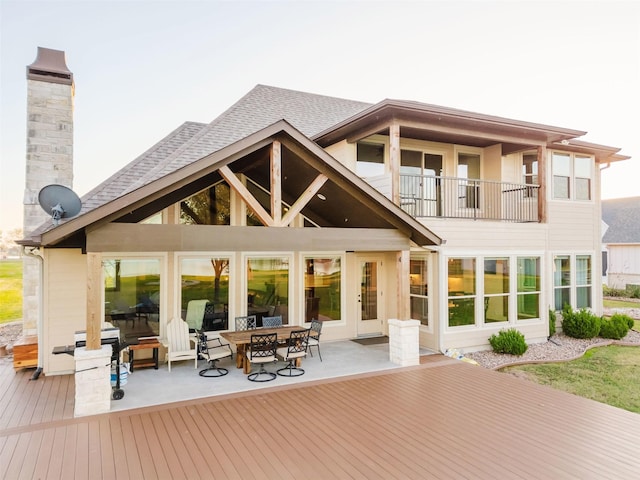 back of house with a balcony, a shingled roof, a chimney, and outdoor dining space