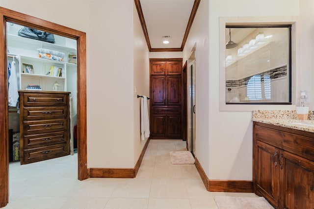 corridor with light tile patterned floors, visible vents, ornamental molding, a sink, and baseboards