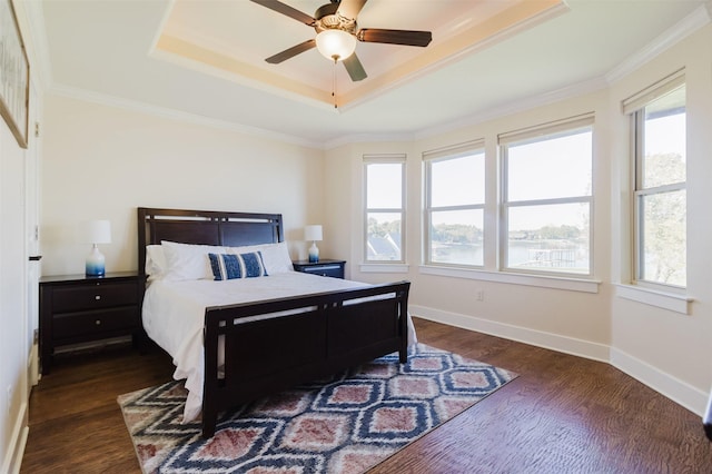 bedroom featuring baseboards, dark wood finished floors, ceiling fan, a tray ceiling, and crown molding