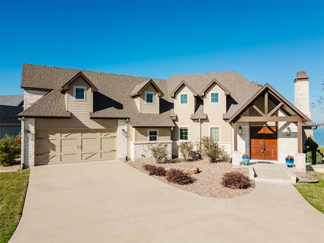 view of front facade with a garage, a shingled roof, driveway, stone siding, and a chimney