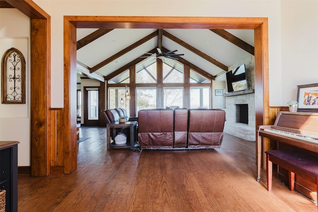 living room with vaulted ceiling with beams, a fireplace, wood finished floors, a ceiling fan, and wainscoting