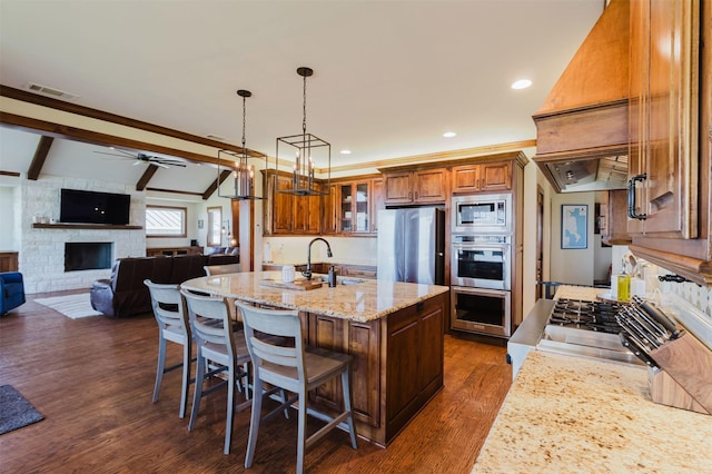 kitchen with a stone fireplace, visible vents, appliances with stainless steel finishes, brown cabinets, and a sink