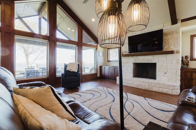 living area featuring a notable chandelier, beam ceiling, wood finished floors, and a stone fireplace