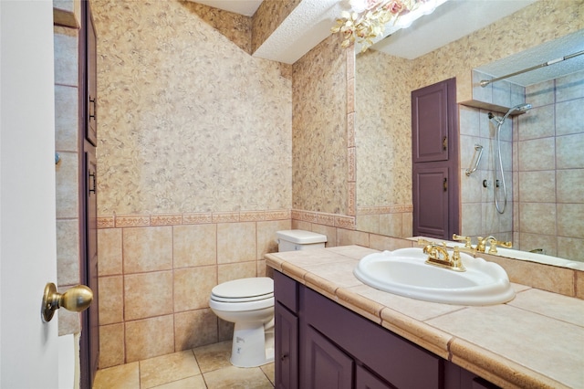 bathroom with vanity, tile patterned flooring, toilet, tile walls, and a tile shower