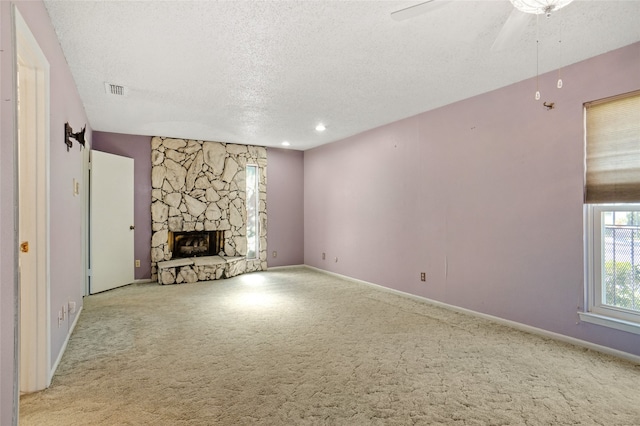 unfurnished living room featuring a stone fireplace, ceiling fan, light colored carpet, and a textured ceiling