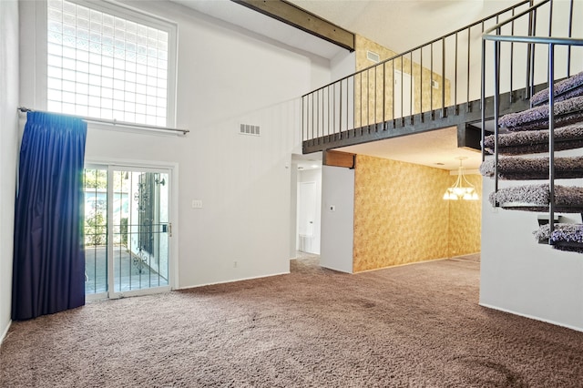 unfurnished living room with carpet flooring, beam ceiling, a towering ceiling, and a chandelier