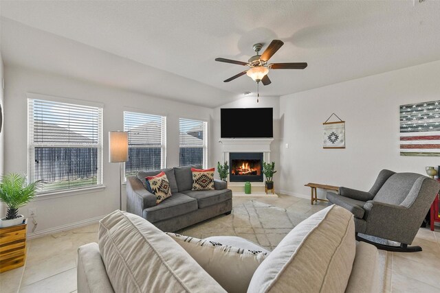 living room with lofted ceiling, a lit fireplace, light tile patterned flooring, baseboards, and ceiling fan