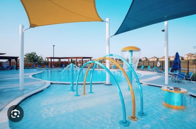 community pool with a patio, fence, and a water play area