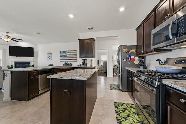 kitchen with light stone countertops, appliances with stainless steel finishes, a center island, and dark brown cabinetry