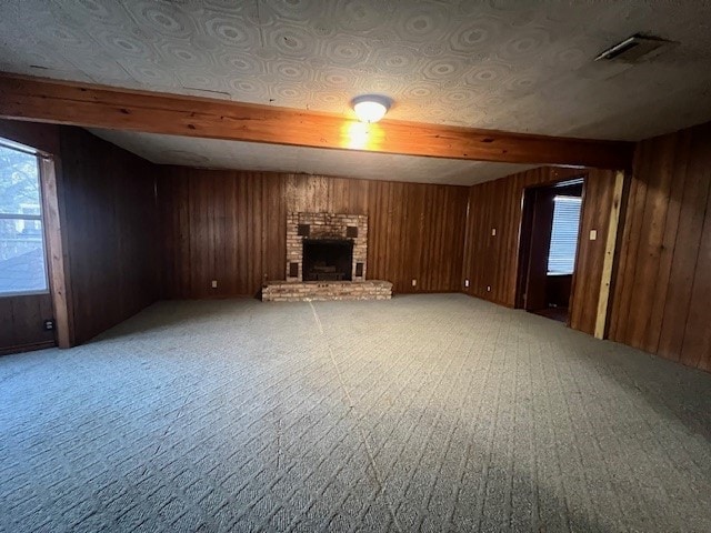 unfurnished living room featuring beamed ceiling, light carpet, wooden walls, and a brick fireplace