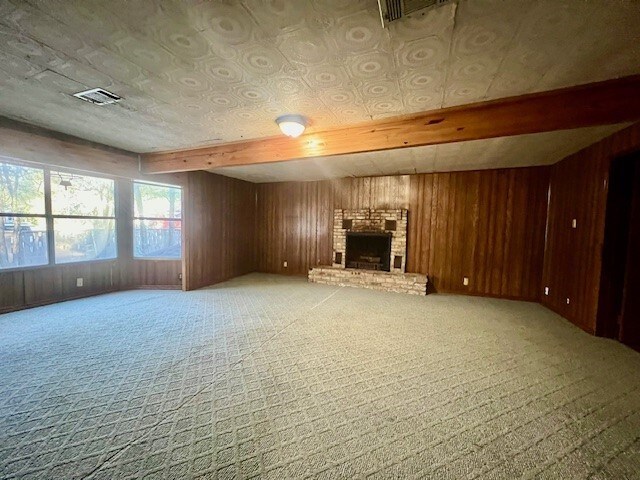 unfurnished living room with wood walls, light carpet, and a brick fireplace