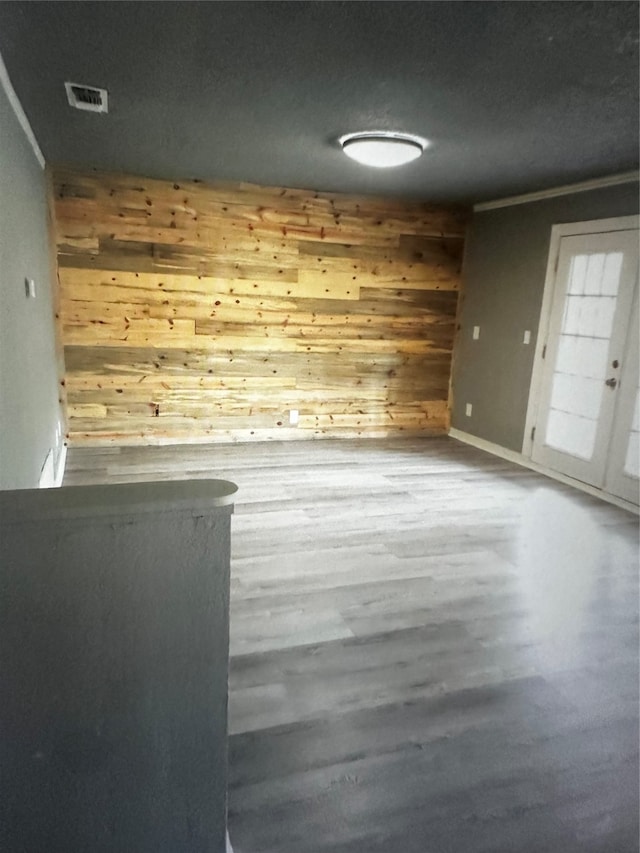 empty room featuring hardwood / wood-style flooring, ornamental molding, and wood walls