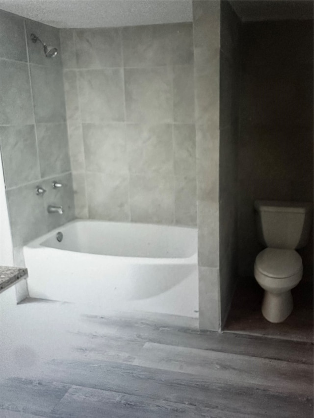 bathroom featuring hardwood / wood-style floors, tiled shower / bath combo, toilet, and a textured ceiling