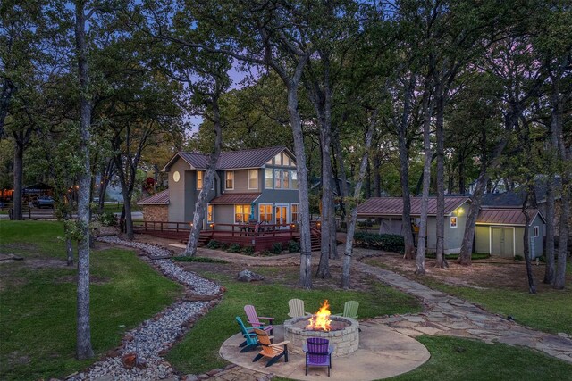 patio terrace at dusk with a water view, a fire pit, and a boat dock