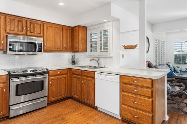 kitchen featuring sink, tasteful backsplash, kitchen peninsula, stainless steel appliances, and light hardwood / wood-style floors