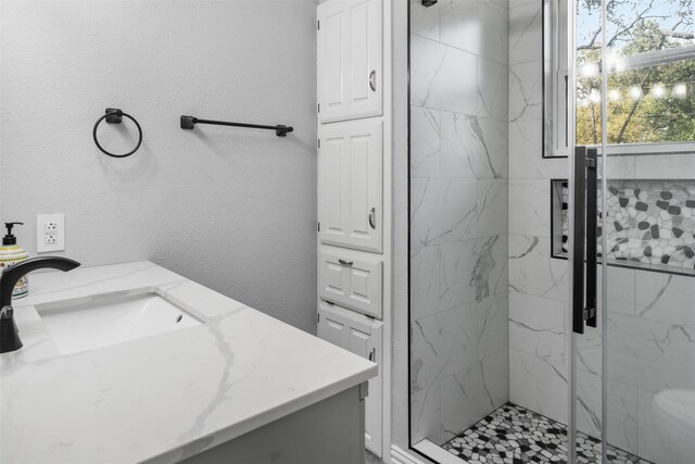 full bath featuring a stall shower, a textured wall, and vanity