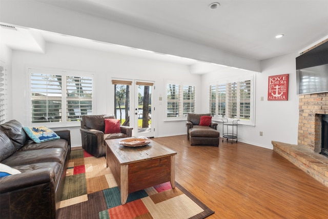 living room with a brick fireplace, hardwood / wood-style floors, and french doors