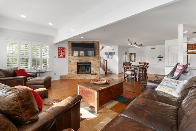 living room with rail lighting, a brick fireplace, and light wood-type flooring