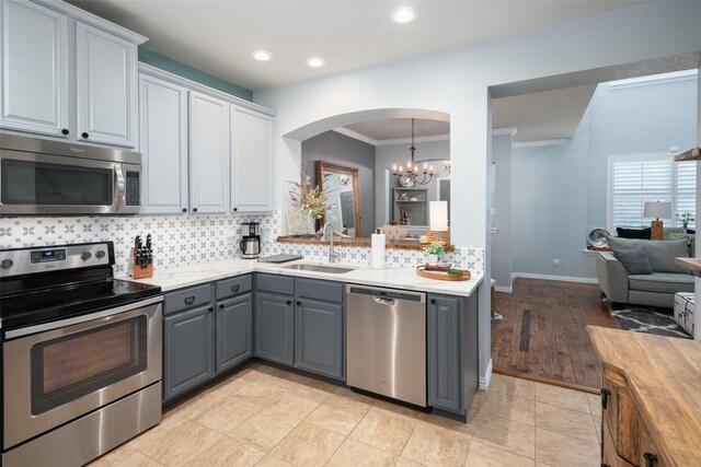 kitchen featuring gray cabinetry, crown molding, sink, appliances with stainless steel finishes, and a notable chandelier