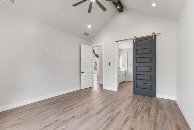 unfurnished bedroom featuring ceiling fan, beam ceiling, a barn door, high vaulted ceiling, and light hardwood / wood-style flooring