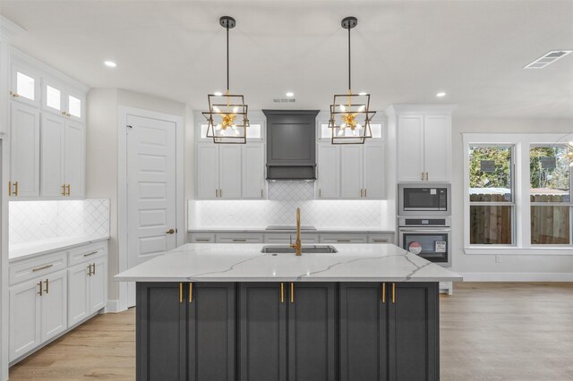 kitchen featuring light stone counters, light hardwood / wood-style flooring, an island with sink, white cabinets, and appliances with stainless steel finishes