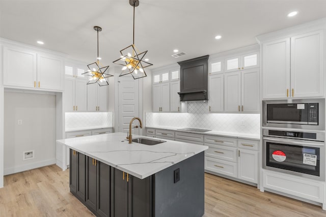 kitchen featuring sink, hanging light fixtures, stainless steel appliances, a kitchen island with sink, and white cabinets