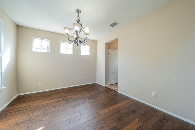 spare room with dark wood-type flooring and an inviting chandelier