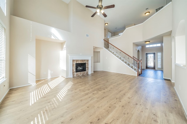 unfurnished living room featuring a tiled fireplace, a towering ceiling, and light hardwood / wood-style flooring