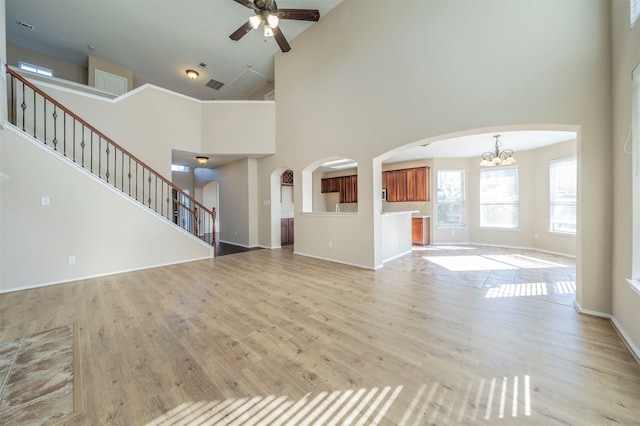 unfurnished living room with ceiling fan with notable chandelier, light hardwood / wood-style floors, and high vaulted ceiling