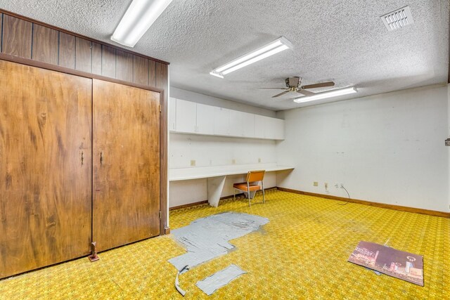 basement with ceiling fan, built in desk, light carpet, and a textured ceiling