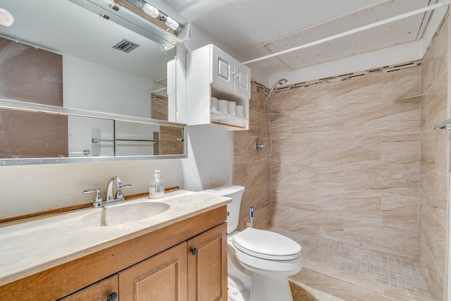 bathroom with a tile shower, vanity, and toilet