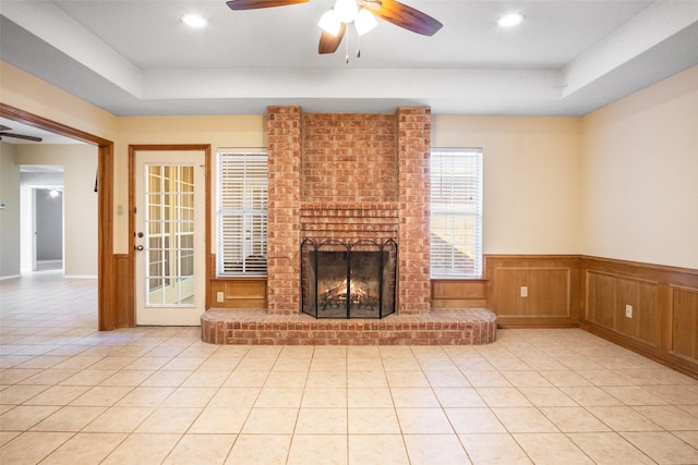 unfurnished living room featuring a fireplace, a raised ceiling, ceiling fan, and light tile patterned flooring