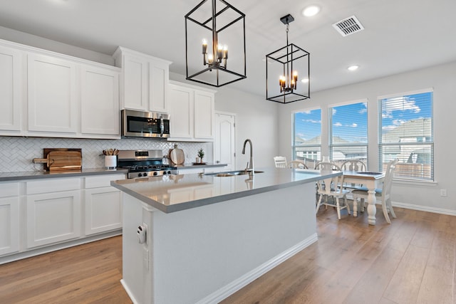 kitchen featuring stainless steel appliances, light hardwood / wood-style floors, decorative light fixtures, a kitchen island with sink, and white cabinets