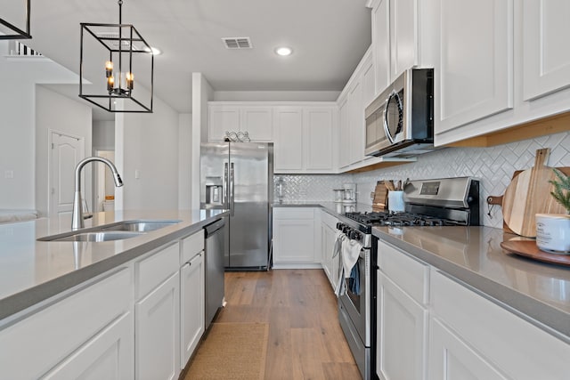 kitchen with white cabinets, sink, appliances with stainless steel finishes, decorative light fixtures, and light hardwood / wood-style floors