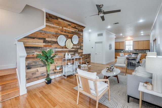 living room featuring wood walls, light hardwood / wood-style flooring, ceiling fan, and ornamental molding