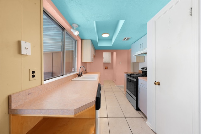 kitchen featuring a textured ceiling, sink, light tile patterned floors, and stainless steel range oven