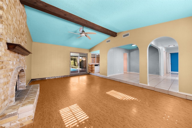 unfurnished living room with lofted ceiling with beams, ceiling fan, light hardwood / wood-style floors, a textured ceiling, and a large fireplace