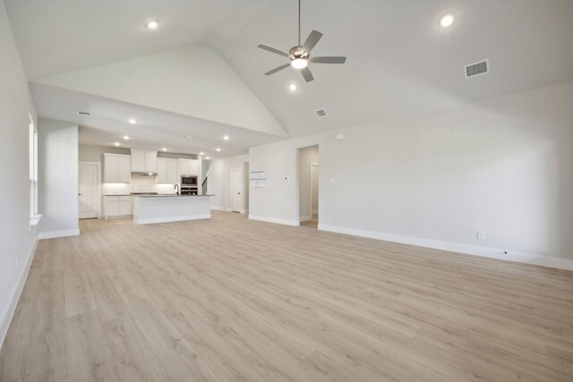 unfurnished living room featuring light wood-type flooring, high vaulted ceiling, ceiling fan, and sink