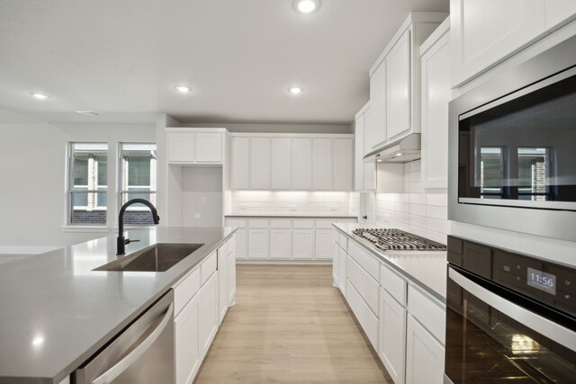 kitchen with light wood-type flooring, tasteful backsplash, stainless steel appliances, sink, and white cabinets