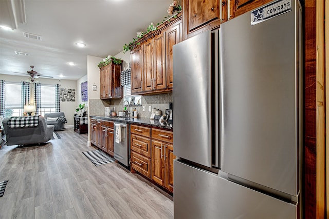 kitchen with dark stone counters, ceiling fan, decorative backsplash, light wood-type flooring, and stainless steel appliances