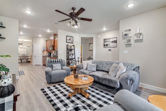 living room featuring ceiling fan with notable chandelier and light hardwood / wood-style floors