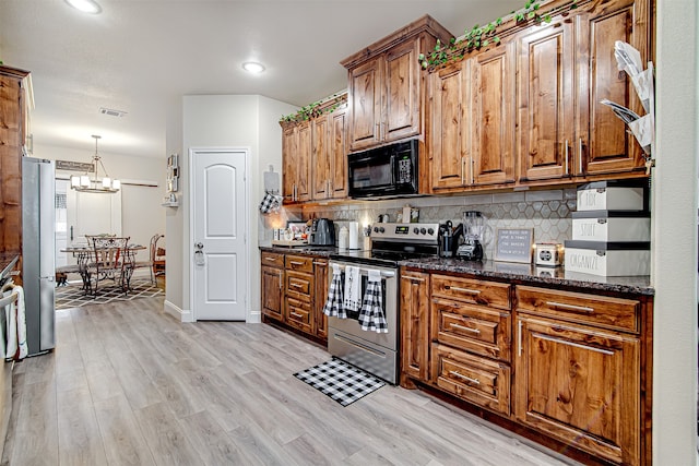 kitchen featuring a chandelier, appliances with stainless steel finishes, light hardwood / wood-style floors, and dark stone counters