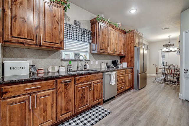 kitchen with light wood-type flooring, sink, dark stone counters, and stainless steel appliances