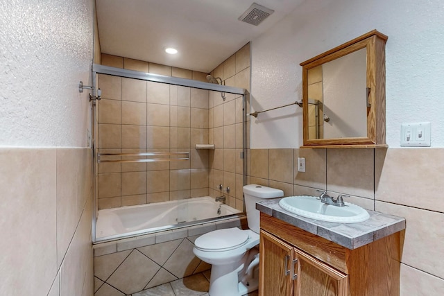 full bathroom featuring toilet, vanity, tile walls, and combined bath / shower with glass door