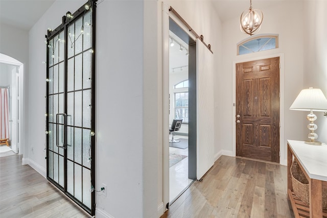 entryway featuring a barn door, light wood-style flooring, baseboards, and a chandelier