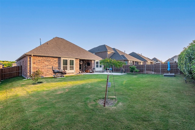 rear view of house featuring a patio, roof with shingles, a fenced backyard, a lawn, and brick siding