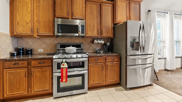 kitchen with dark stone countertops, light colored carpet, backsplash, and appliances with stainless steel finishes