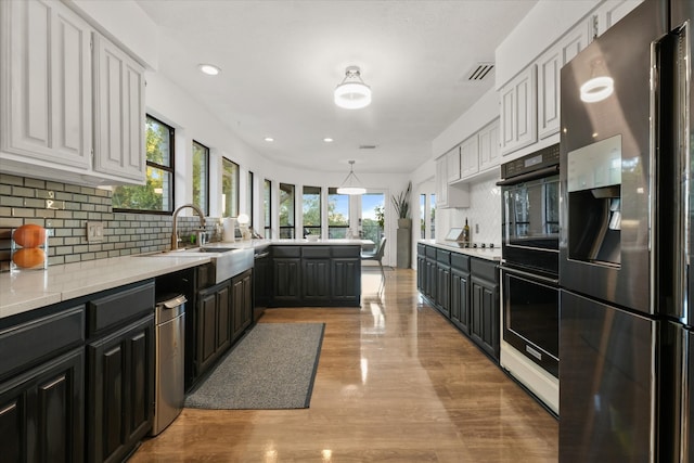 kitchen featuring appliances with stainless steel finishes, backsplash, light hardwood / wood-style flooring, white cabinetry, and hanging light fixtures