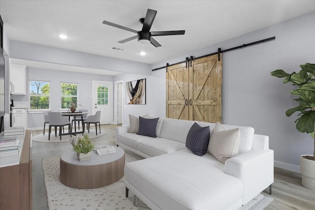 living room featuring light hardwood / wood-style floors, a barn door, and ceiling fan