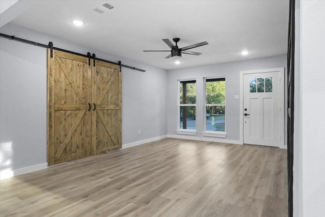 unfurnished living room with light hardwood / wood-style floors, a barn door, and ceiling fan